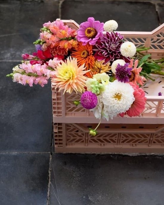 Een grote mand met een veelkleurig bloemboeket, waaronder roze leeuwenbekjes, dahlia's en zinnia's in een roze krat.