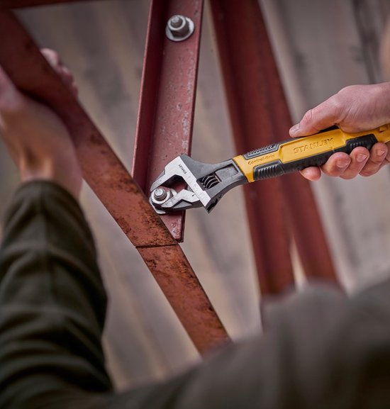 Stanley verstelbare moersleutel met geel-zwarte grip wordt gebruikt om een bout aan een roestig metalen frame vast te draaien.