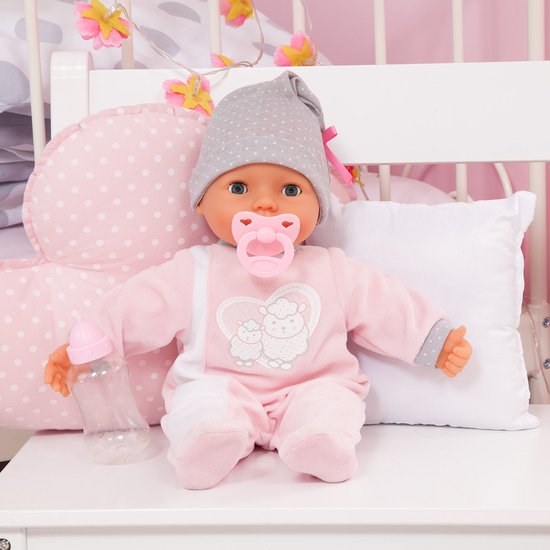 Babypop in roze slaappakje met grijze stippenmuts, met flesje, zittend op een bedje.