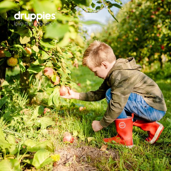 Jongen met rode laarzen, zittend in een boomgaard, plukt appels.
