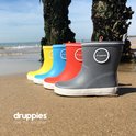 Grijze, rode, blauwe en gele rubberen regenlaarzen met witte zolen op het strand.