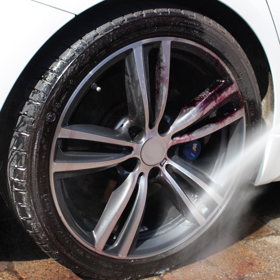 Une jante de voiture est nettoyée sous pression d'eau, avec un liquide rouge qui coule.