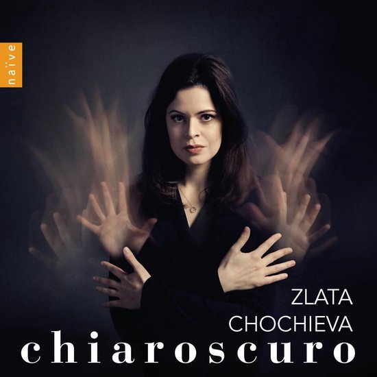 Zlata Chochieva - Chiaroscuro. Vrouw met donker haar en donkere kleding, met etherische handen om haar heen.
