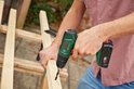 Man met gestreepte blouse boort in een houten constructie met een groene Bosch boormachine.