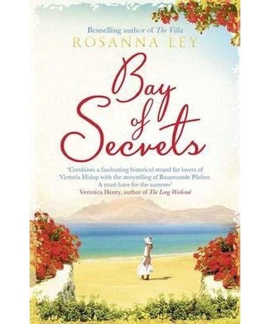 Couverture du livre 'Bay of Secrets' de Rosanna Ley. Une femme en robe blanche se tient sur une plage près de la mer, entourée d'arbustes rouges fleuris et de murs en pierre. Le titre est en lettres rouges.