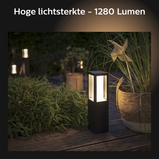 Zwarte vierkante staande buitenlamp met wit licht, met 1280 lumen, naast een grote plant met windmolen.