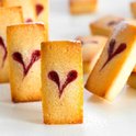 Close-up van gouden gebakjes met hartvormige rode jam erop, bestrooid met poedersuiker.