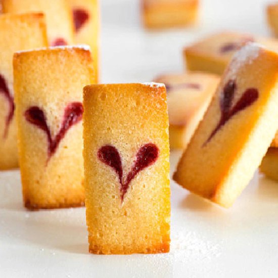 Close-up van gouden gebakjes met hartvormige rode jam erop, bestrooid met poedersuiker.