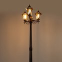 Een drielichts lantaarnpaal in de kleur goud/messing met verlichte lampen, tegen een donkere achtergrond.