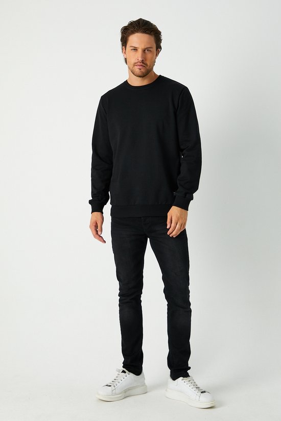 Vue complète d'un homme aux cheveux bruns portant un pull noir, un jean noir et des baskets blanches.