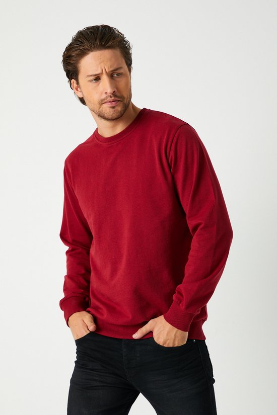 Homme portant un sweat bordeaux à col rond et pantalon noir, mains dans les poches.
