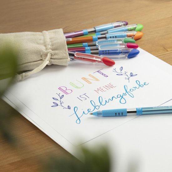 Een schetsboek met de tekst 'BUNT IST MEINE lieblingsfarbe' in veelkleurige letters. Een blauwe pen ligt erop, naast een zak met kleurrijke pennen.
