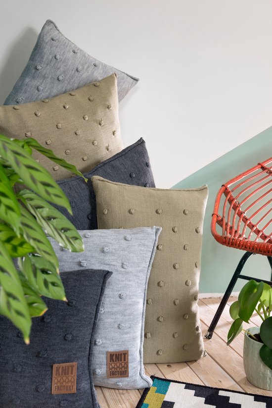 Stapel kussens met bolletjespatroon in grijs, beige en donkergrijs. Een plant op de voorgrond.