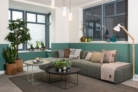 Groen hoekbankkussen met diverse decoratieve kussens en plaids in bruin-, grijs- en beige tinten.