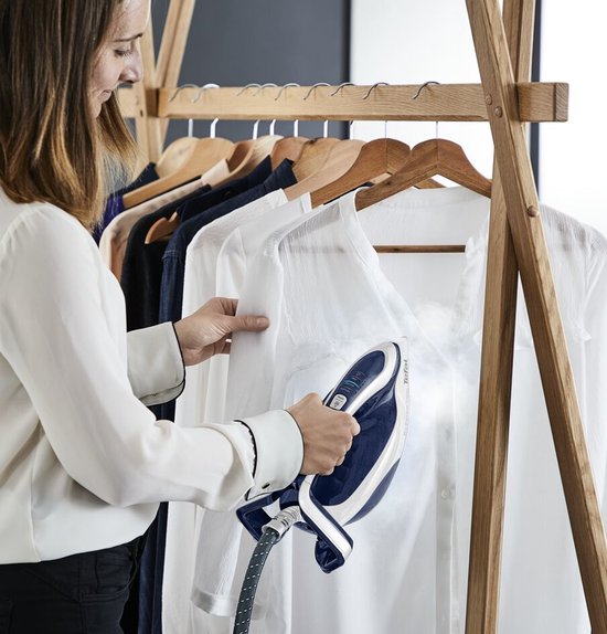 Vrouw met witte blouse stoomt een witte blouse met de donkerblauwe Tefal stoomgenerator.