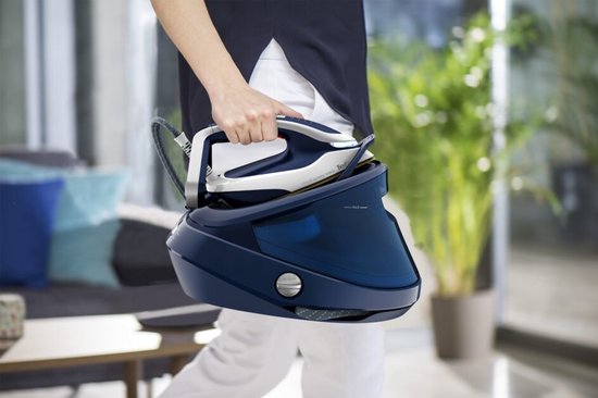 Persoon in donkerblauwe top en witte broek draagt het donkerblauwe Tefal Pro Express Vision stoomstrijkijzer.
