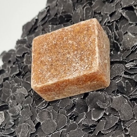 Een bruin, korrelig amberblokje op een zwarte, schilferige ondergrond.