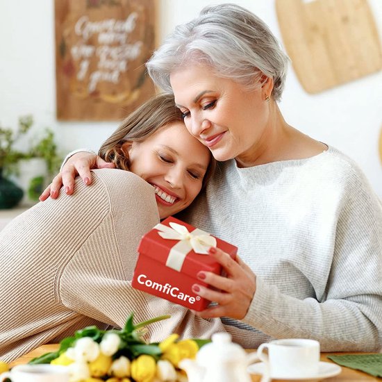 Vrouw met grijzend haar omhelst een jongere vrouw die een rood geschenkdoosje met de tekst ComfiCare vasthoudt.
