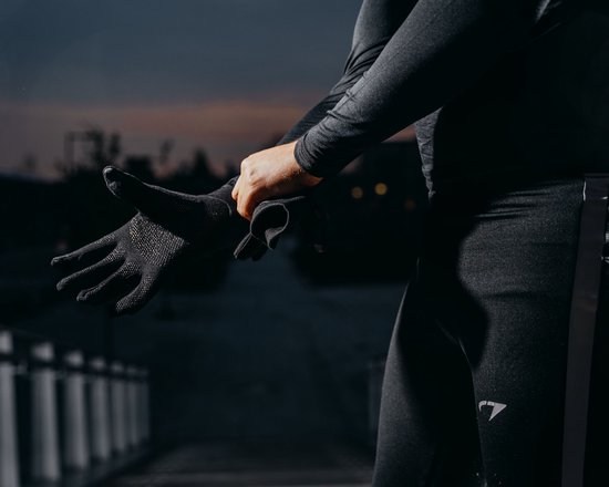 Persoon trekt zwarte Avento sporthandschoenen aan in de schemering. De handschoenen hebben een antislipprint op de palm.