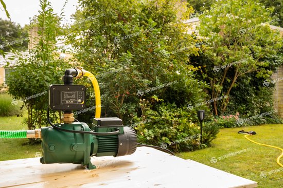 Groene DAB jet waterpomp met zwarte control-d unit en gele slang, geplaatst op een houten tafel in een tuin.