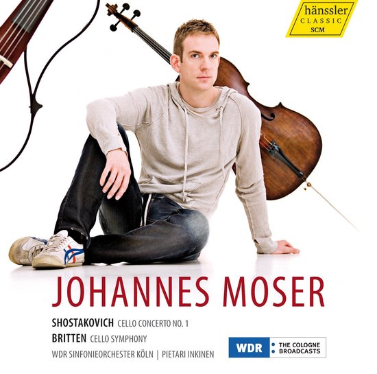 Johannes Moser zit naast een cello met een hoodie en jeans.