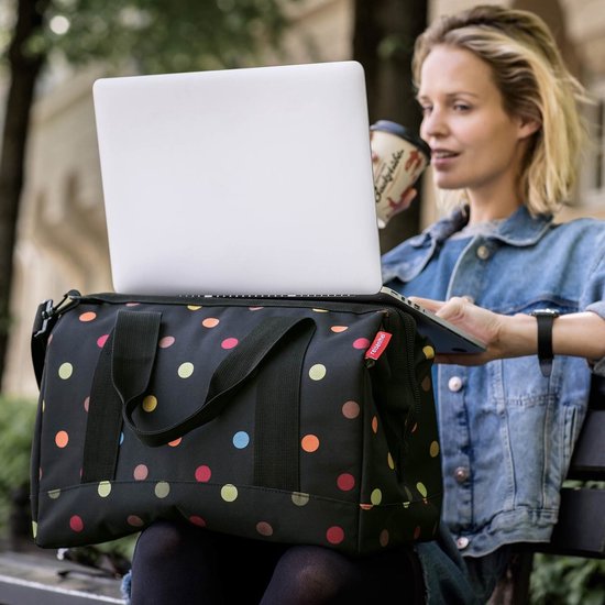 Vrouw met sproeten en sproeten zit op een bankje met een laptop en een tas met stippen.