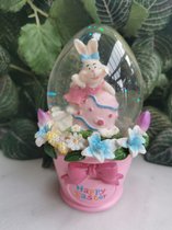 Shaker ovale de décoration de Pâques de 12,5 cm de haut avec un œuf de Pâques décoré rose et un joyeux lapin qui vous salue dans une robe rose avec un nœud bleu sur un seau rose décoré de fleurs printanières
