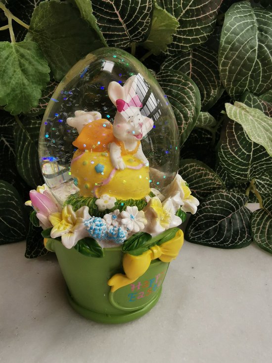 Paasdecoratie  ovale  schudbol van 12.5 cm hoog met spelend konijntje op paasei in groen emmertje met bloemen - Merkloos