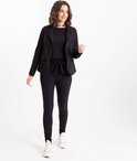 Model met zwarte blazer, zwart shirt en zwarte slim fit broek met strikceintuur.