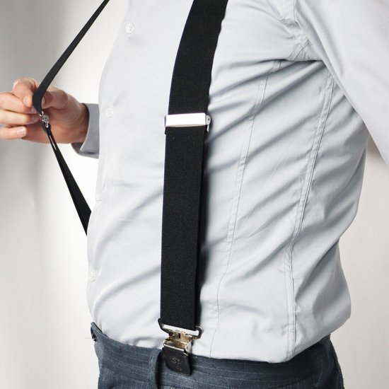 Man in lichtgrijs overhemd en jeans met zwarte bretels en zilverkleurige clips.