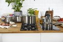 Een keuken aanrecht met verschillende RVS pannen op een inductiekookplaat. Er liggen ook groenten en pasta.