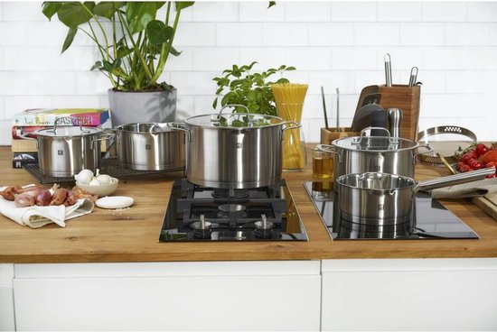 Een keuken aanrecht met verschillende RVS pannen op een inductiekookplaat. Er liggen ook groenten en pasta.