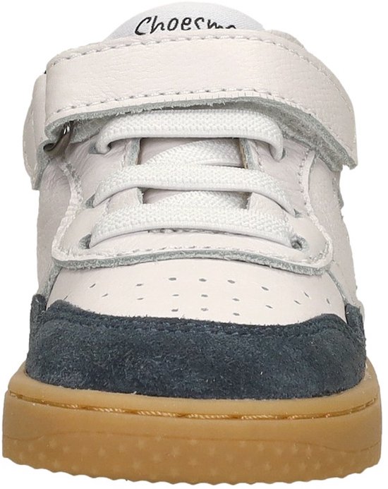 Voorkant van een witte sneaker met blauwe suède accenten, klittenband en veters.