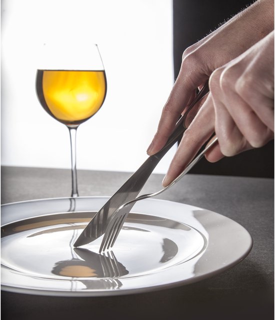 Mains coupant dans une assiette blanche avec un couteau et une fourchette, avec un verre de vin blanc à côté.