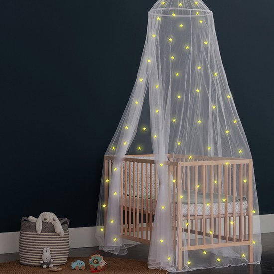 Witte tule klamboe met gele gloeiende sterren, gedrapeerd over een houten babybedje.