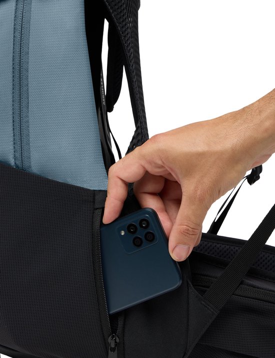Hand plaatst smartphone in een mesh zijvak van een blauwgrijze rugzak.