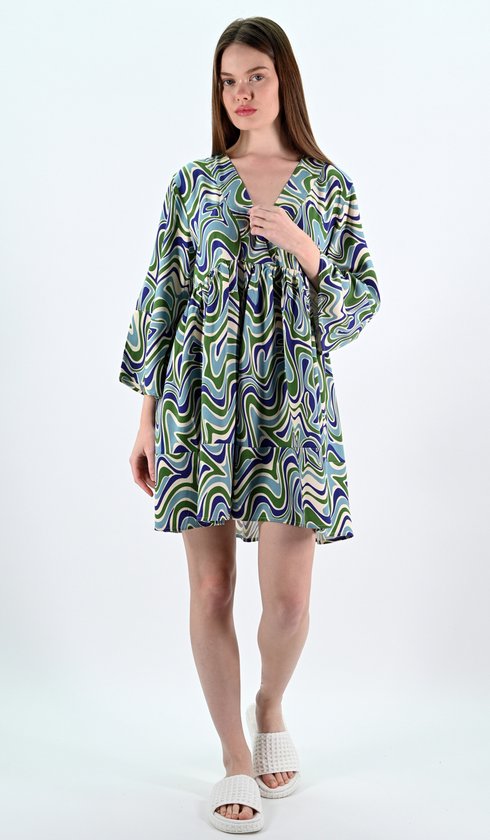 Mannequin portant une robe courte à motif ondulé, décolleté en V et manches longues évasées. Elle porte ses mains sur sa poitrine.