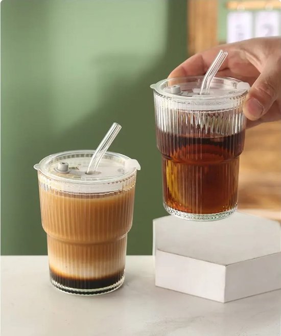 Une main saisit un gobelet cannelé avec couvercle et paille, rempli de thé glacé et de citron, à côté d'un gobelet de café stratifié.