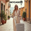 Vrouw met een beige outfit en zonnebril loopt met een champagne koffer door een straat. Logo SKYCASE.