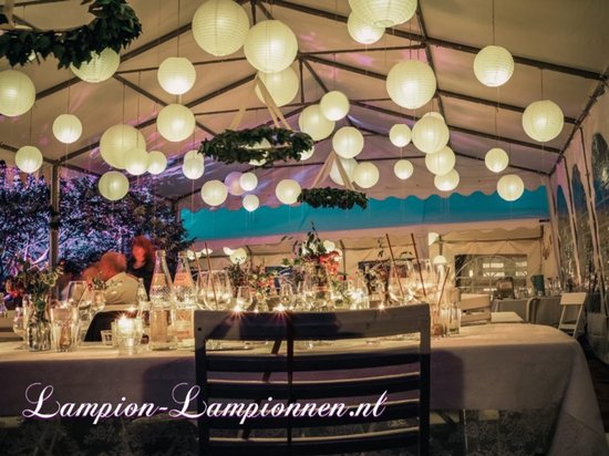 Bruiloftstent ingericht met witte papieren lampionnen, tafels en stoelen.