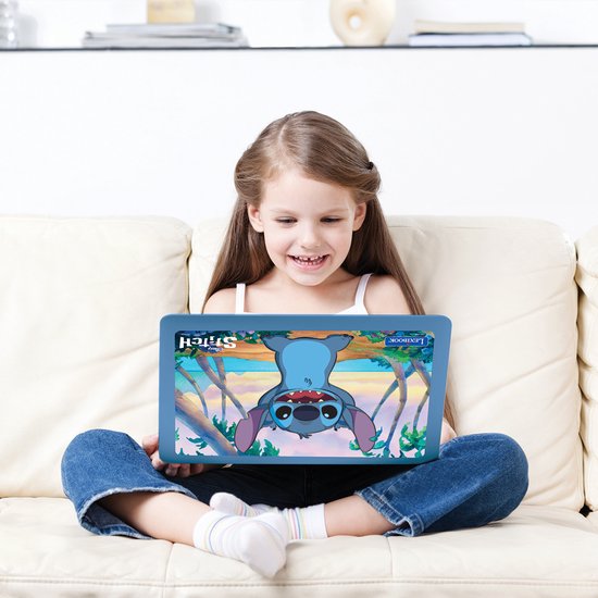 Een lachend meisje zit op een bank en houdt een blauwe Lexibook laptop met Stitch erop vast.