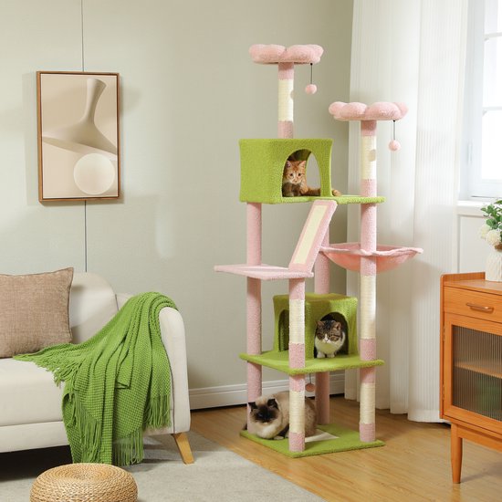 Hoge krabpaal met roze en groene platformen, huisjes en hangmand, in een woonkamer. Een kat zit in een huisje, een andere ligt in de hangmand.