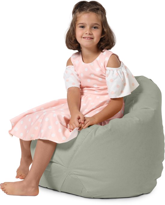 Meisje met bruin haar in roze jurk met witte stippen zit op een grijze zitzak.