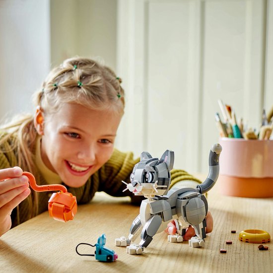 Fille construisant un chat LEGO sur une table avec une tablette et une souris jouet.