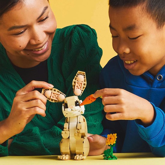 Femme et enfant construisent un lapin LEGO avec carotte.