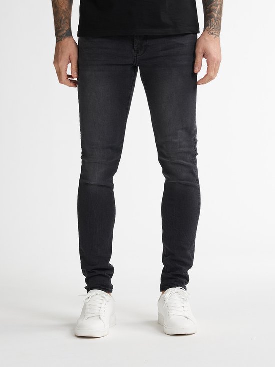 Onderlichaam van een man, voorkant, met strakke zwarte spijkerbroek en witte sneakers.