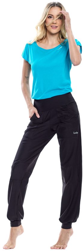 Model in een zwarte, comfortabele joggingbroek met een elastische tailleband en logo op de heup. Ze draagt een turquoise T-shirt.