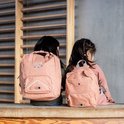 Twee meisjes zitten op een houten bankje. Het linker meisje draagt een roze rugzak met kattengezicht.