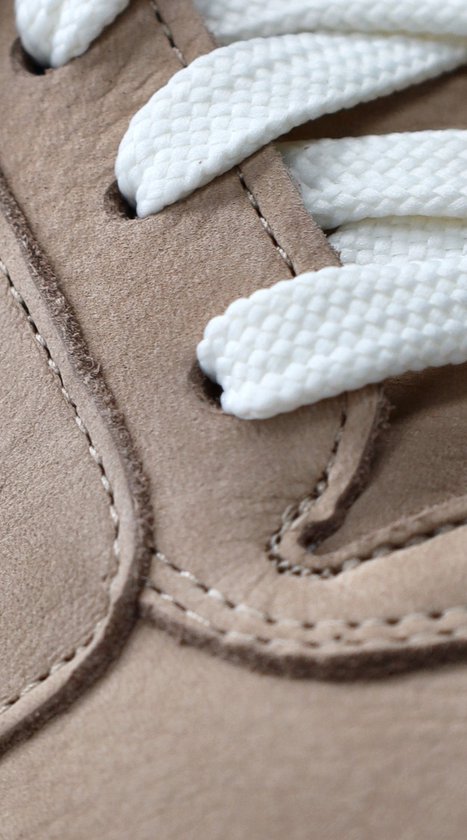 Close-up van lichtbruine leren sneaker met witte veters en stiksels.