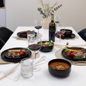 Gedekte tafel met zwarte borden, wijnglazen, bestek en een fles rode wijn.